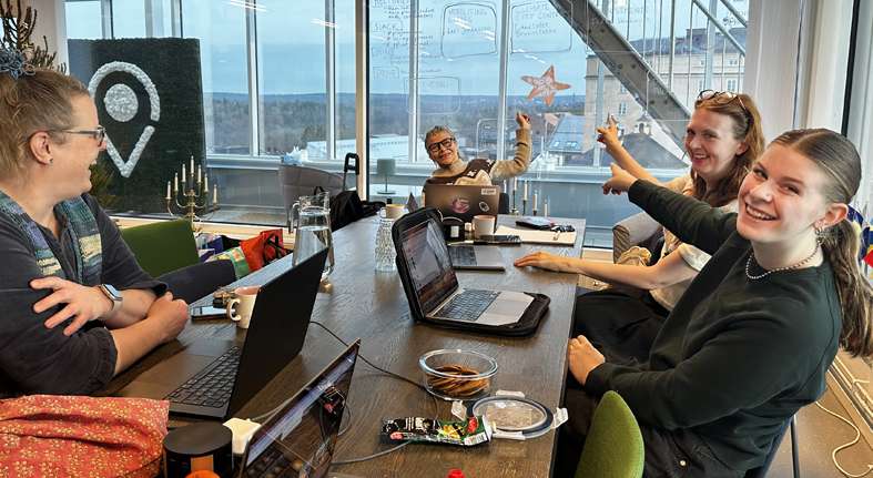 Four people in an office pointing upward at a starfish decoration, laptops and coffee on table